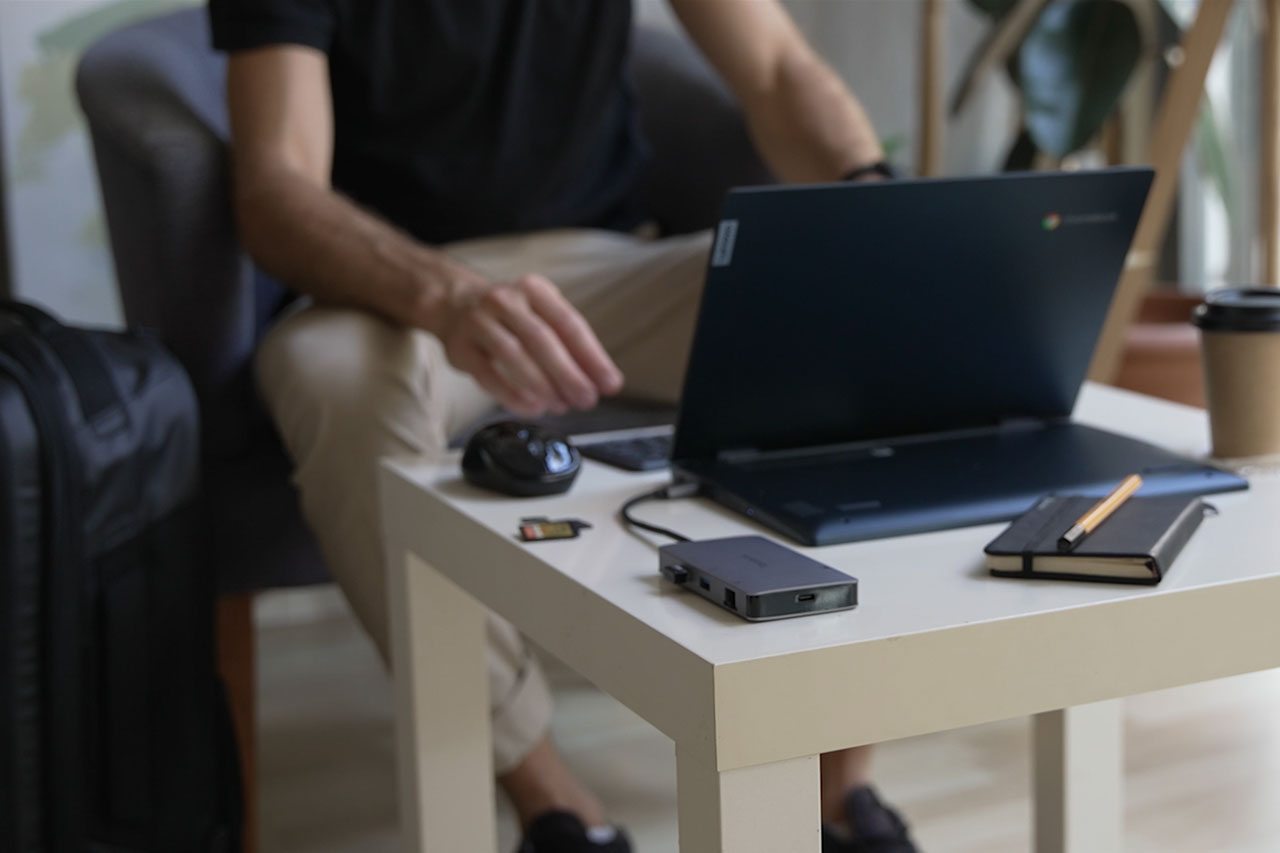 person working in a hotel lobby using a laptop, prortable dock and wireless mouse.